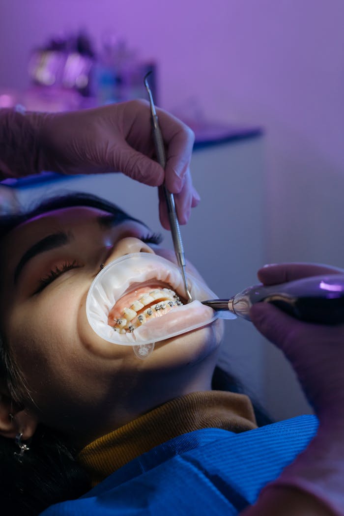 Dentist performing orthodontic procedure on patient with braces in a clinic setting.